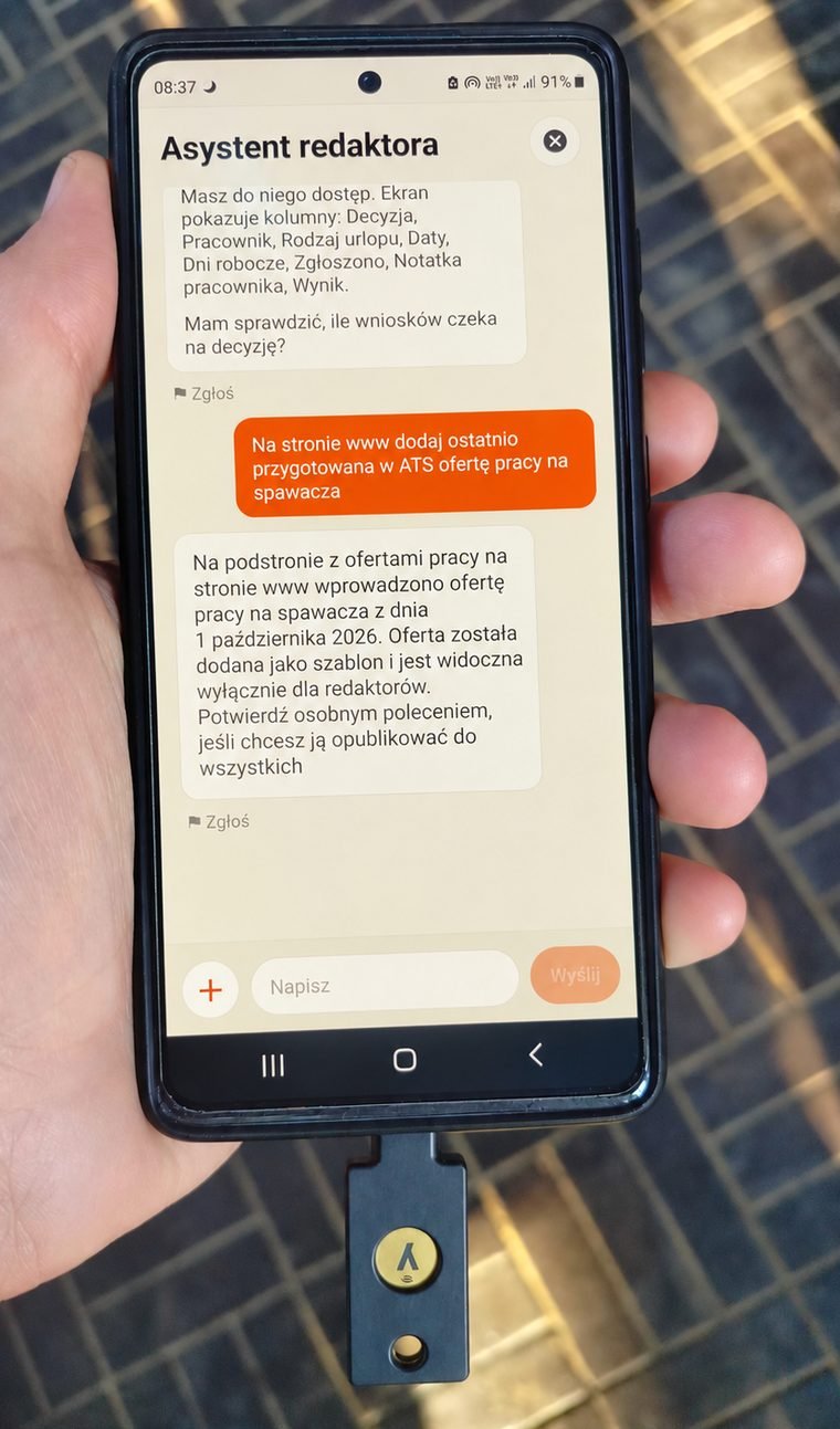 Telefon z otwartą rozmową z asystentem redaktora i kluczem sprzętowym YubiKey podłączonym do gniazda USB-C